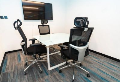 Small meeting room with a white table, mesh ergonomic chairs, and a wall-mounted TV.