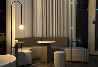 Communal lounge area with curved beige seating, a round pedestal table, and a modern arc floor lamp.