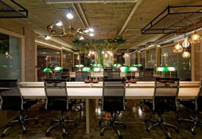 Large office area with rows of desks, mesh chairs, and warm decorative lighting fixtures.