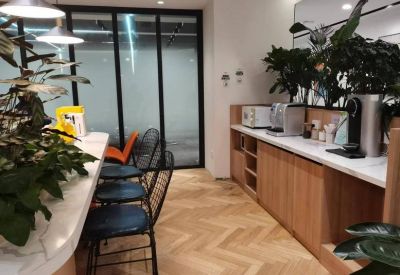 A modern pantry area with wooden cabinets, coffee machines, and blue bar stools.