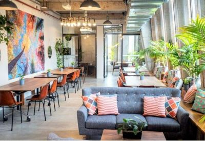 Bright coworking area featuring a large colorful mural, blue sofa, and indoor plants.