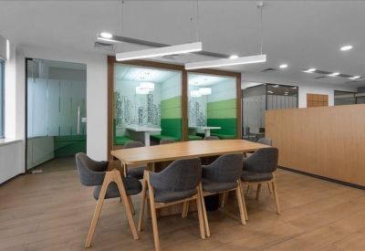 Collaborative workspace with a large wooden table and gray chairs near private booths.
