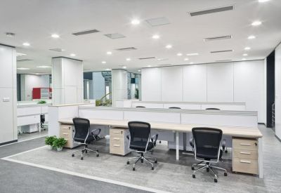 Spacious open-plan office with white desks and black ergonomic chairs.