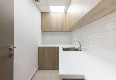 Clean communal kitchen area with white countertops and light wood cabinetry.