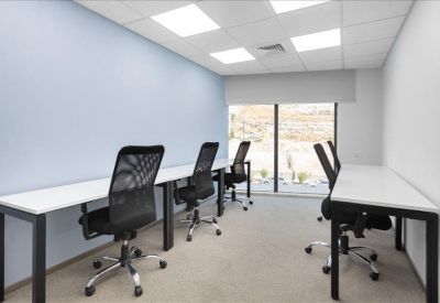 Bright coworking area with white desks and black mesh chairs by a large window.