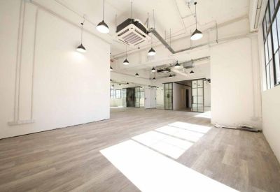 Large empty open-plan office space with light wood flooring and industrial ceilings.