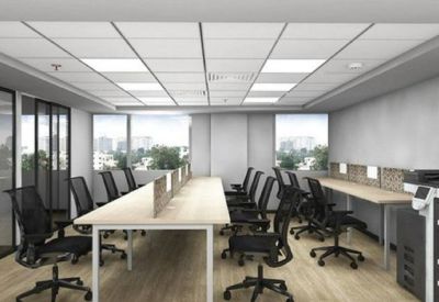 Bright open-plan office with multiple rows of workstations, ergonomic black chairs, and window views.