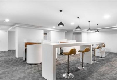 Communal breakout area with a long white high-top table and tan bar stools.