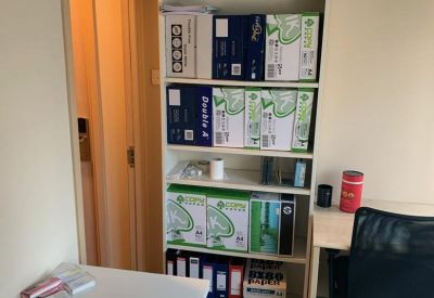 Shared office space featuring a tall white bookshelf stocked with supplies and binders.