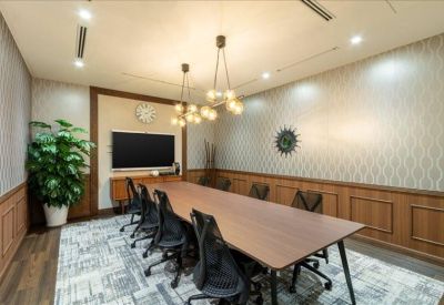Meeting room with long wooden table, black ergonomic chairs, and a large wall-mounted monitor.