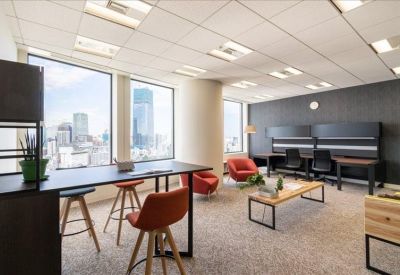 Bright coworking area with bar-height seating, orange chairs, and floor-to-ceiling city views.
