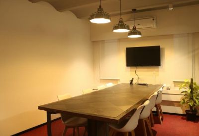Meeting room with a long table, wall-mounted TV, and hanging lights.