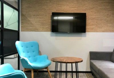 Small meeting nook with turquoise wingback chairs, a round wooden table, and a wall-mounted screen.