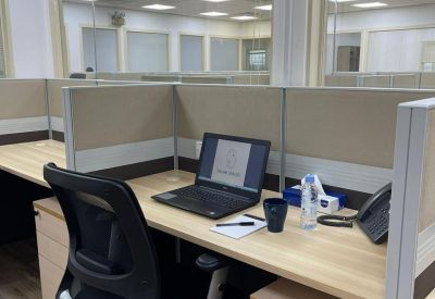 Cubicle workstation with a light wood desk, ergonomic chair, and laptop setup.