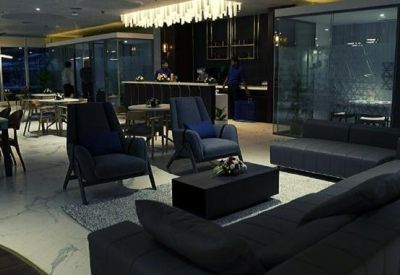 Contemporary lounge with plush dark sofas, a coffee station, and marble flooring.