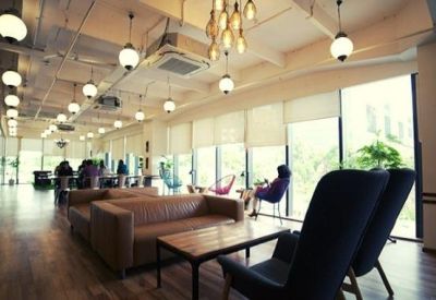 Bright coworking space with leather sofas, wooden flooring, and large windows with natural light.