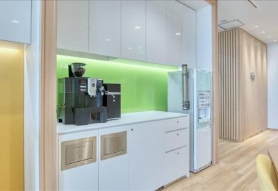 Communal kitchen area with a coffee machine, refrigerator, and clean white cabinetry.