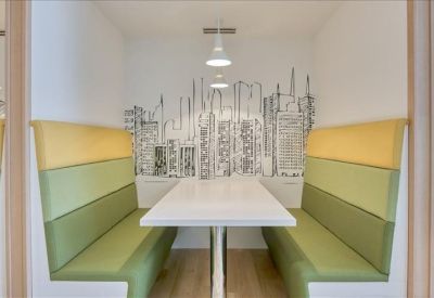 Private meeting booth with comfortable green and yellow padded seating and city wall art.