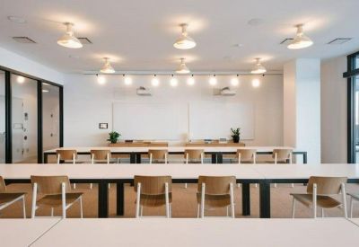 Bright meeting room with white long tables and rows of wooden chairs.