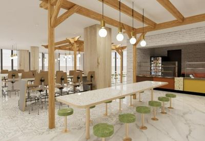 Bright open-plan office space with long white desks, green stools, and warm timber ceiling beams.