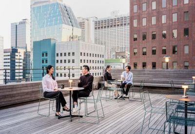 Rooftop terrace with wooden decking and people sitting at tables against a city skyline.