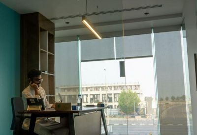 Sunlit communal area with large windows, a wooden desk, and views of the city.