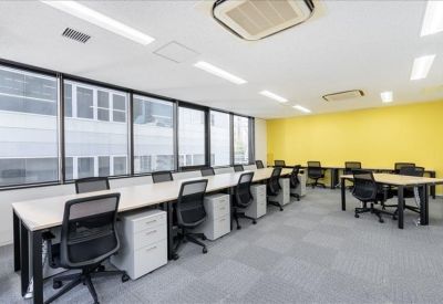 Open-plan workspace with rows of white desks, black chairs, and a yellow feature wall.