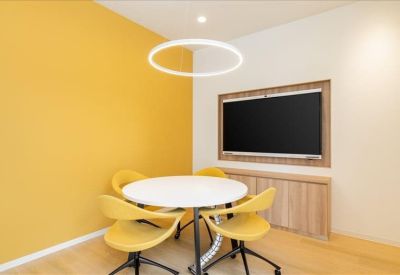 Small meeting room with a round table, yellow chairs, and a wall-mounted screen.