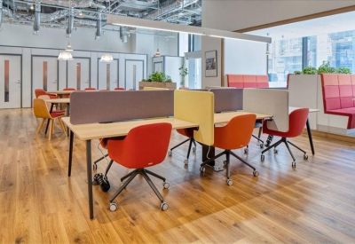 Open-plan coworking space with colorful red and orange chairs and wooden flooring.