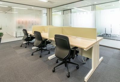 Semi-private workstations with light wood desks and black ergonomic chairs behind glass partitions.