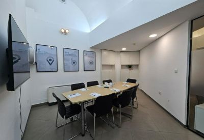 Small meeting room with a wooden table, black chairs, and framed artwork on white walls.