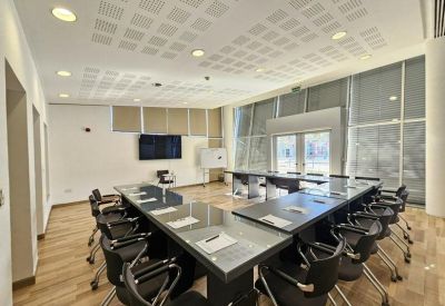 Large boardroom featuring a U-shaped table arrangement and grid-patterned ceiling tiles.