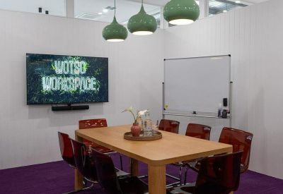 Meeting room with a long wooden table, orange chairs, and green pendant lights.