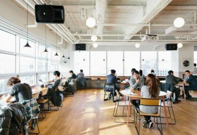 Spacious open-plan office area with light wood floors and diverse seating arrangements.
