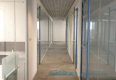 Bright office corridor with glass partitions and a grid-style ceiling.