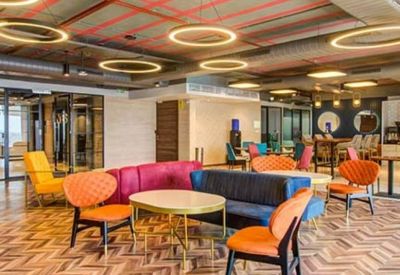 Spacious communal lounge with colorful seating, herringbone wood floors, and circular light fixtures.