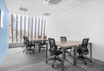 Bright four-person private office with wooden desks and black ergonomic chairs.