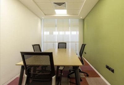 Bright meeting room with a long wooden table, black mesh chairs, and a green accent wall.