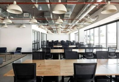 Wide-angle open-plan workspace with multiple desks, black chairs, and large windows.