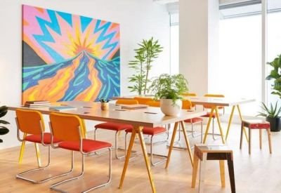 Bright meeting area featuring a long wooden table, orange chairs, and a colorful sunrise painting.