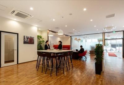 Bright communal coworking space with a large high-top table, wooden floors, and potted plants.