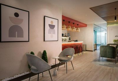 Reception lounge with stylish grey armchairs, abstract wall art, and a coffee bar in the background.