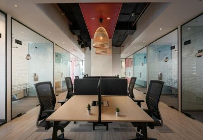 Coworking space featuring long shared desks, ergonomic chairs, and warm pendant lighting.