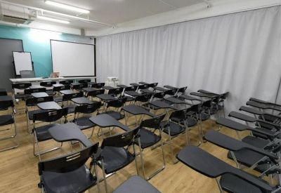 Large training room with rows of black tablet arm chairs and a projection screen.