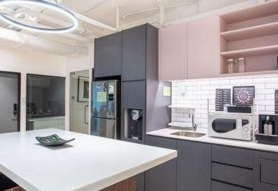 Modern communal kitchen area with grey and pink cabinetry and a white island.
