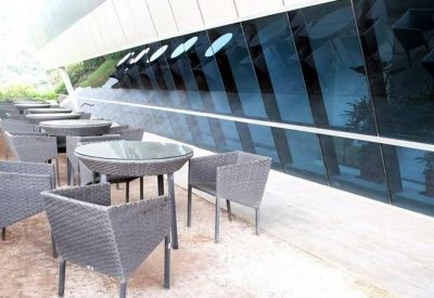 Outdoor terrace seating with woven chairs and circular glass tables alongside a modern glass facade.