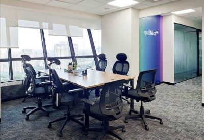 Office workspace featuring ergonomic mesh chairs and a long wooden desk by large windows.