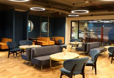 Reception lounge with grey sofas, blue chairs, and herringbone wood flooring.