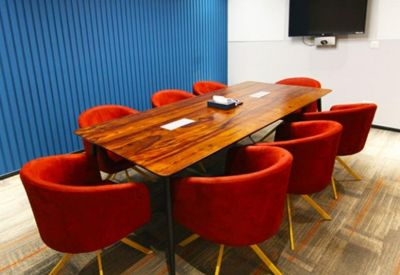 Modern meeting room featuring a long wood table, red velvet armchairs, and a blue slated feature wall.
