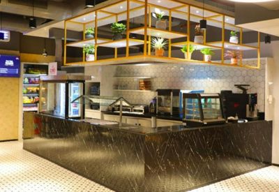 Modern cafe area with a dark marble counter and a hanging gold shelf unit with potted plants.